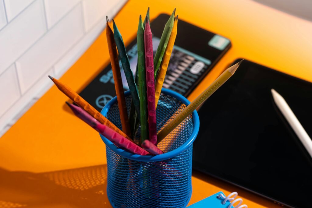Vibrant pencils in a holder with school supplies on an orange desk, perfect for educational themes.